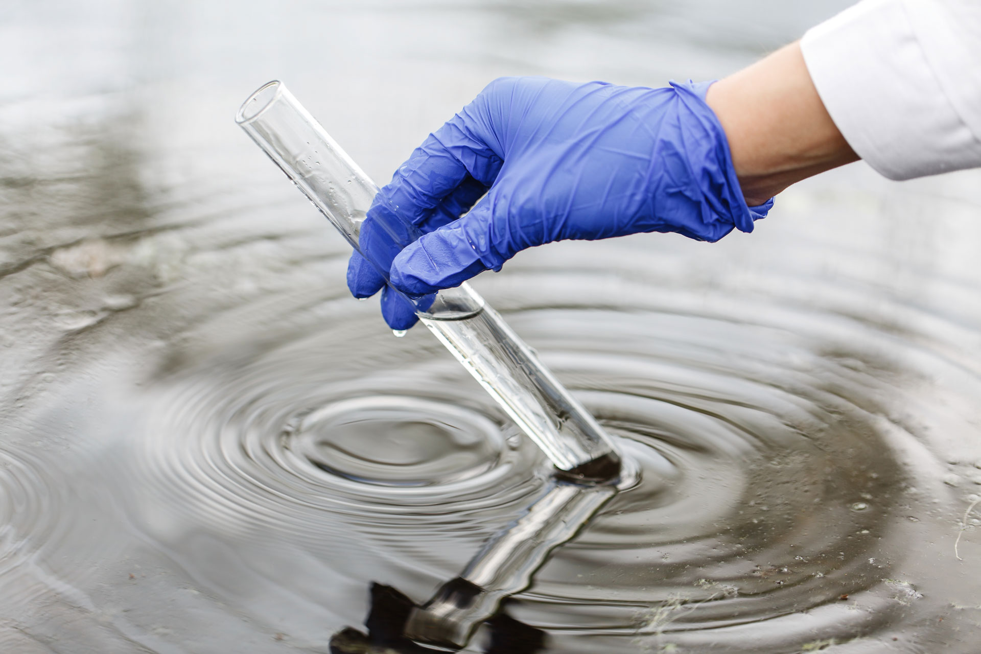 investigador-sostiene-tubo-ensayo-agua-mano-guante-azul
